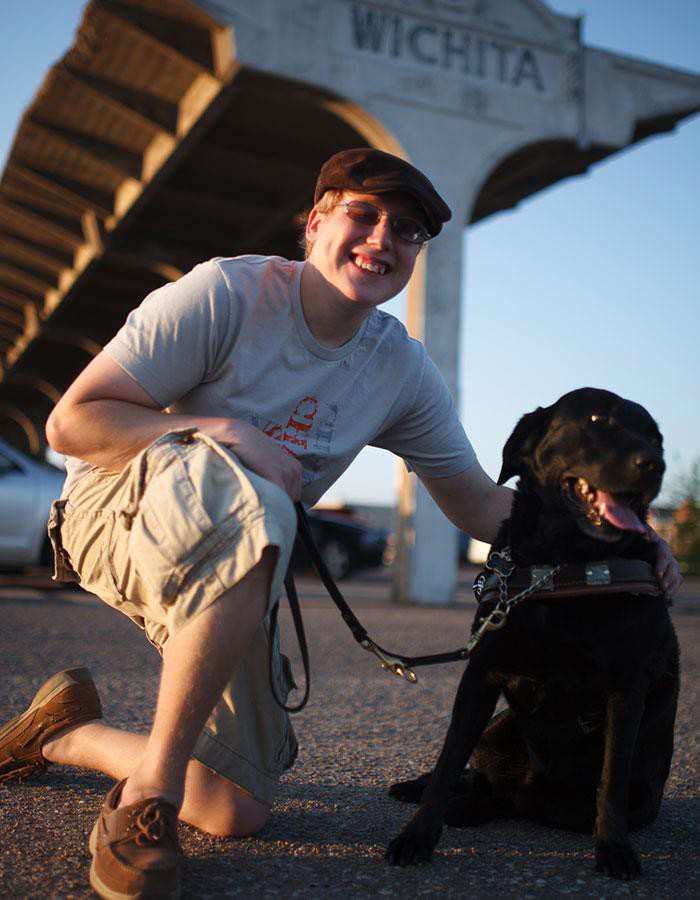 photo of Andrew with a black lab guide dog and Wichita parking roof span in the background