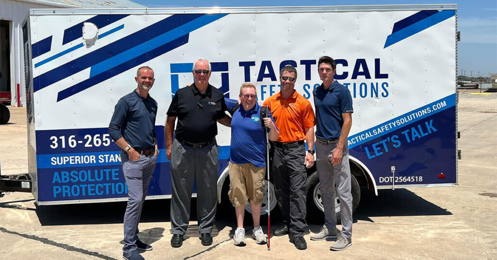 photo of founder Andrew Crane standing in front of Guiding Paws' Into the Light trailer with with reps from sponsor Tactical Solutions